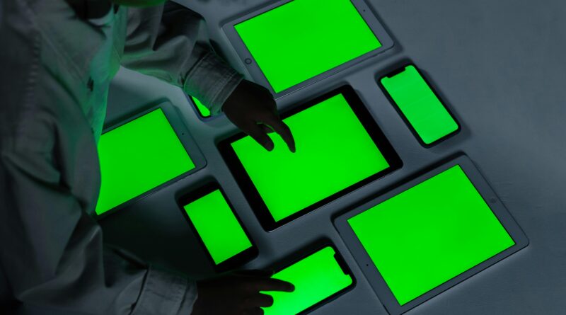 A variety of electronic gadgets with green screens being interacted with indoors.